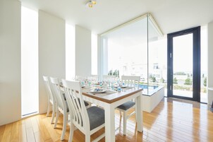 Un comedor con mesa de madera dispuesta para una comida, sillas blancas y un ventanal que ofrece vistas al exterior.