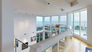 Un intérieur spacieux avec de grandes fenêtres donnant sur la mer, un balcon avec des sièges d’extérieur et un escalier moderne.
