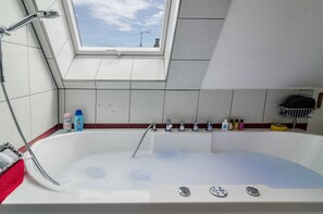 A bathroom with a skylight, a bathtub, a showerhead, and toiletries on the wall. - Vacation Apartment "Flair Lilie" Shared Garden, Sauna & Jacuzzi (Stockach)