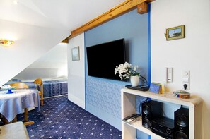 A room with a TV mounted on the wall, a small table with a chair, a bed with a blue bedspread, and a speaker system. - Vacation Apartment "Flair Lilie" Shared Garden, Sauna & Jacuzzi (Stockach)