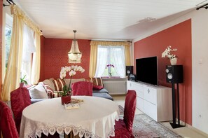 A room with a round dining table, a sofa, a TV, and a speaker.