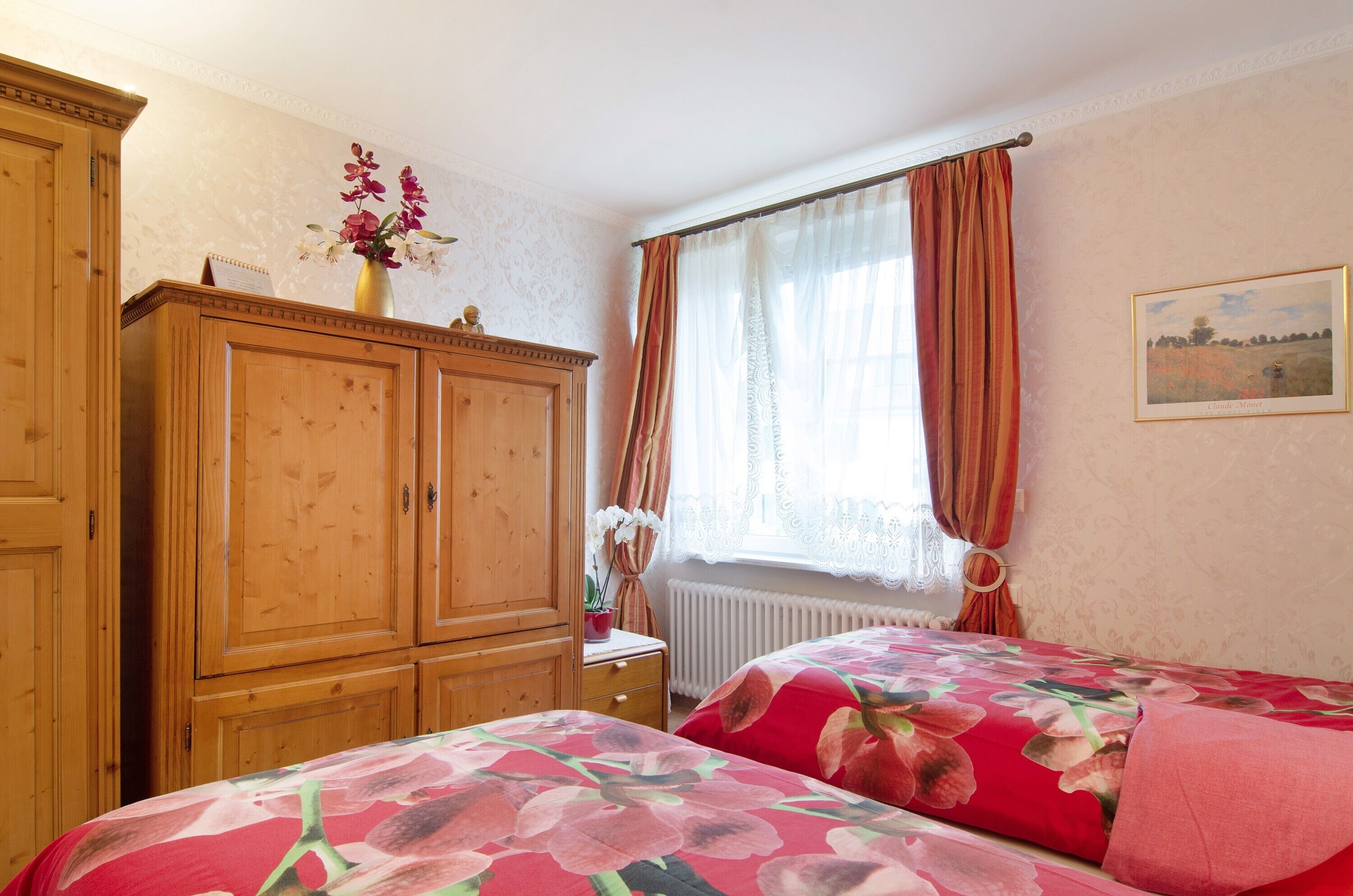 Une chambre avec deux lits, une armoire en bois, un radiateur et une fenêtre avec des rideaux.