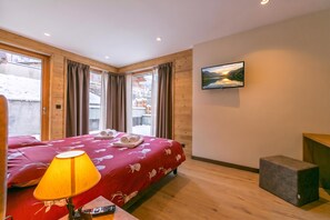 A hotel room with a bed, a desk, a lamp, a TV, and a view of a snowy landscape. - Casa Giardino Ski in - Ski out 100m, Livigno, Italy (Livigno)
