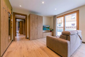 Un salon moderne avec un canapé, un téléviseur et une vue sur un immeuble par une grande fenêtre.