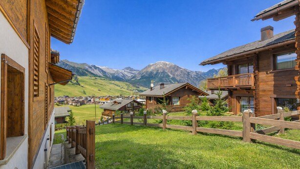 Un chalet de madera con balcón, cerca de madera y vistas a las montañas.