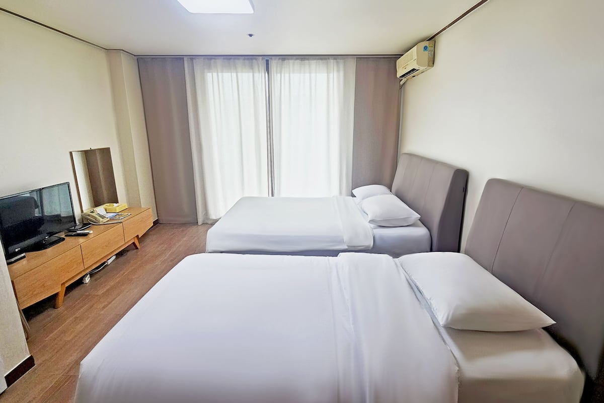 Une chambre d’hôtel avec deux lits, une télévision, une commode en bois et une fenêtre avec des rideaux.
