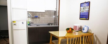 Cocina compacta con refrigerador, lavamanos y una pequeña mesa de comedor con sillas. En la pared, se exhibe un calendario.