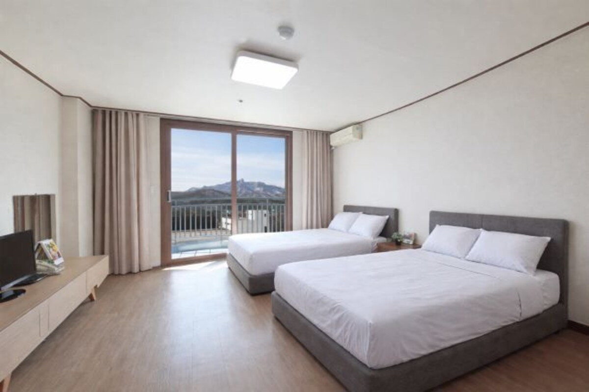 A hotel room with two beds, a TV, a desk, and a balcony with a mountain view.