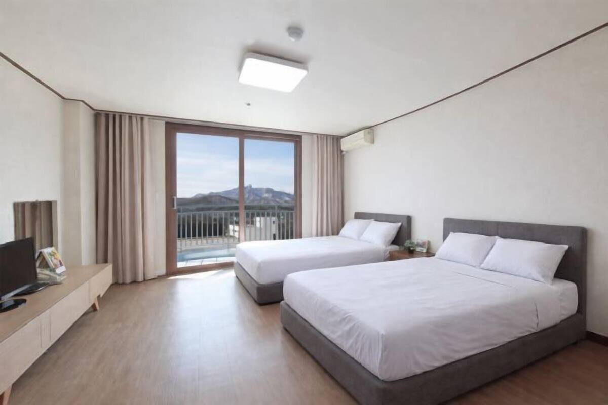 Une chambre d’hôtel avec deux lits, une télévision, un bureau et un balcon offrant une vue sur la montagne.