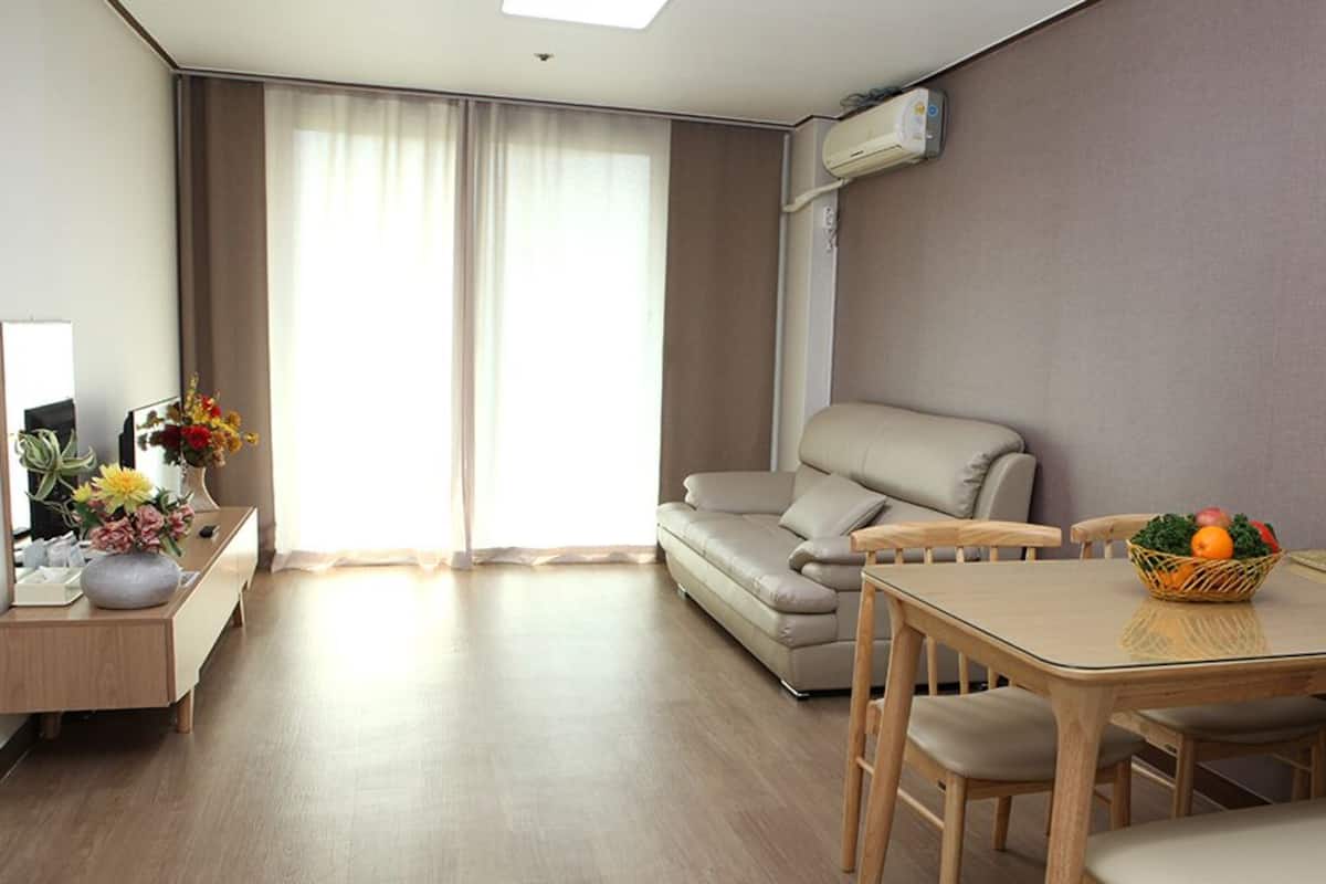 Une chambre d’hôtel moderne équipée d’un canapé, d’une table à manger avec des chaises, d’un petit bureau agrémenté d’un vase de fleurs et d’un climatiseur fixé au mur.