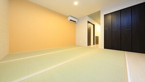 Ein Zimmer mit Tatami-Matten, einem Holzschrank und einer Klimaanlage.