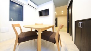 Ein kleiner Essbereich mit einem runden Tisch und vier Stühlen, einer Klimaanlage, einem flachbildfernseher an der Wand und einer dunklen Holzkommode.