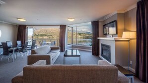 Habitación de hotel con un ventanal amplio que ofrece vistas a la montaña, un televisor de pantalla plana montado en la pared y una chimenea.