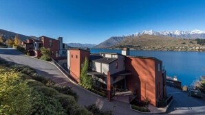 Una zona residencial moderna con casas contemporáneas, un cielo azul despejado y un lago con montañas al fondo.