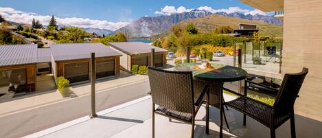 A modern outdoor patio with a table and chairs, overlooking a mountainous landscape and a clear blue sky.