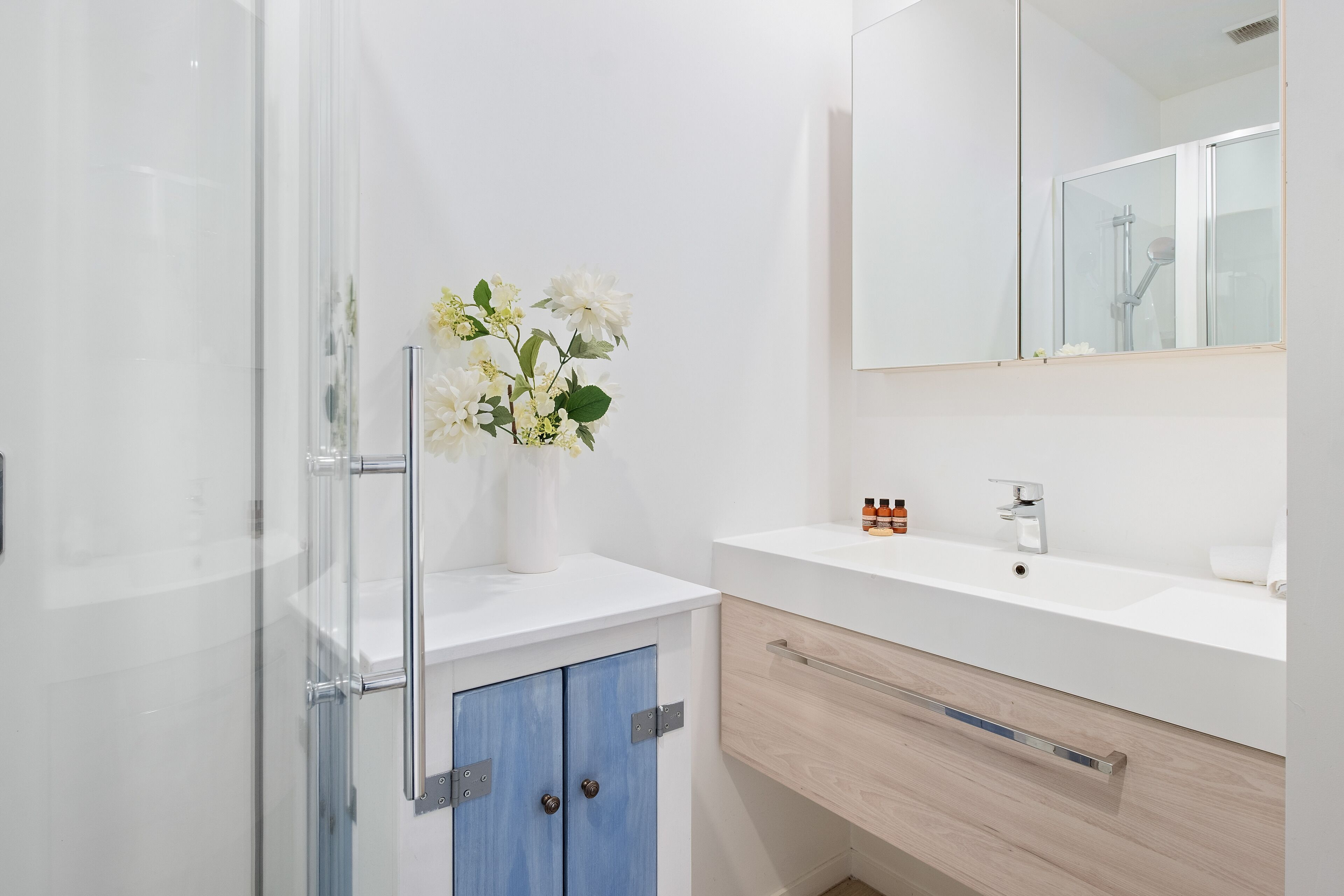 A modern bathroom with a glass shower enclosure, a white sink, and a mirror above it.