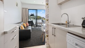 A modern kitchen with a large window, a dining area with a black sofa and chairs, and a view of a mountain landscape. - Brookside Gem Modern 2 Bedroom Apartment (Queenstown)