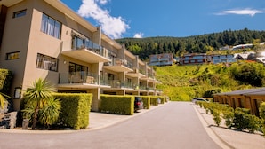 A modern multi-story hotel with balconies, a clear sky, and a hilly backdrop. - Brookside Gem Modern 2 Bedroom Apartment (Queenstown)