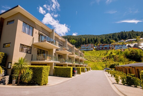 A modern multi-story hotel with balconies, a clear sky, and a hilly backdrop. - Brookside Gem Modern 2 Bedroom Apartment (Queenstown)