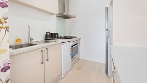 A compact kitchen with white cabinets, a stainless steel sink, a built-in oven, and a refrigerator. - Brookside Gem Modern 2 Bedroom Apartment (Queenstown)