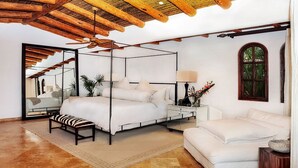A spacious bedroom with a four-poster bed, a sitting area with a sofa, a large mirror, and a ceiling fan. - Exclusive Beachfront Villa with Private Pool Awaits You (Cabo San Lucas)