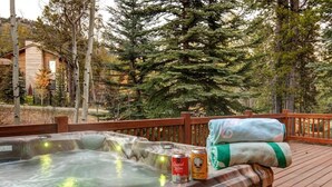 A hot tub with a wooden deck, surrounded by trees and a building in the background. - Abode at the Homestead, walk to slopes, hot tub (Teton Village)