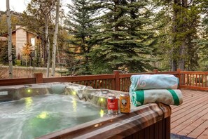 Un jacuzzi con terraza de madera, rodeado de árboles y un edificio al fondo.