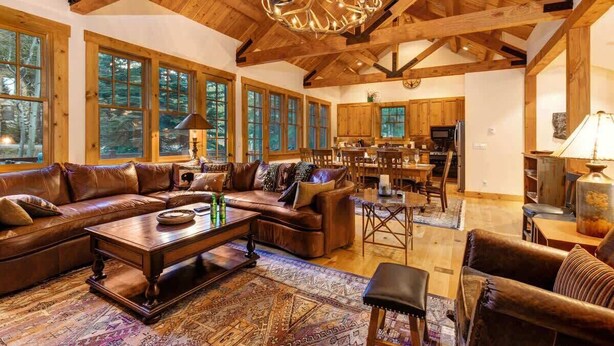 A spacious living room with a large brown leather sofa, a wooden coffee table, and a chandelier. - Abode at the Homestead, walk to slopes, hot tub (Teton Village)