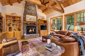 Una sala de estar acogedora con chimenea de piedra, muebles de cuero y un amplio ventanal con vistas al exterior.