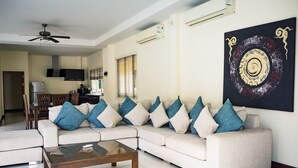 A living room with a sectional sofa, a glass coffee table, and a ceiling fan. - Villa Tanya at Platinum (Rawai)