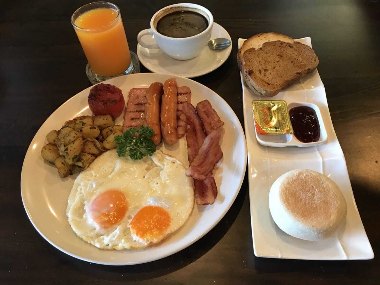 En frukosttallrik med ägg, bacon, korv, potatisbullar, rostat bröd och en kopp kaffe.