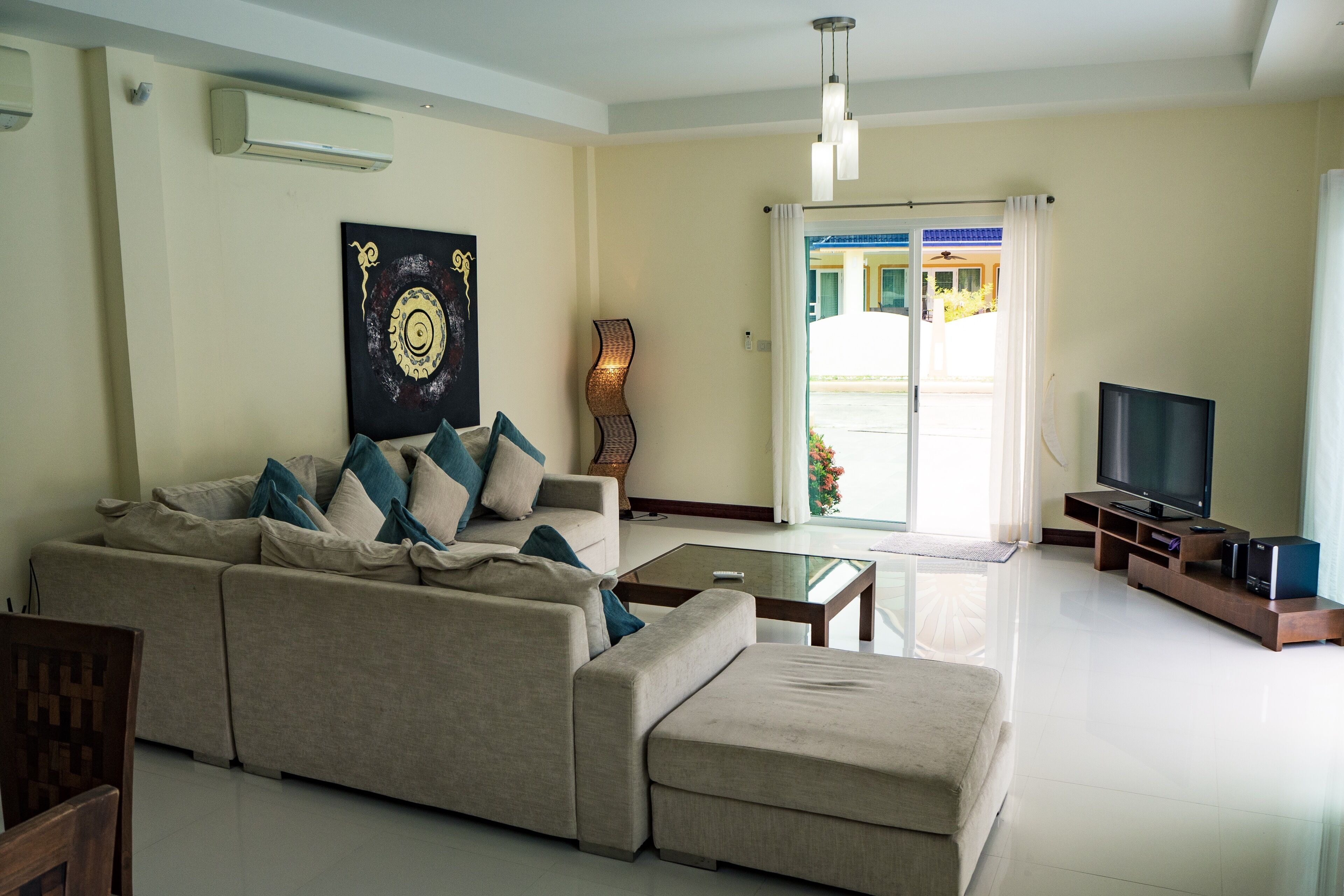 A modern living room with a large sofa, a glass coffee table, a flat-screen TV, and a decorative wall piece.
