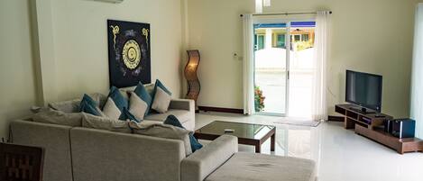 A modern living room with a large sofa, a glass coffee table, a flat-screen TV, and a decorative wall piece.