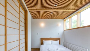 Une chambre moderne avec un mur en lambris de bois, un lit avec une literie blanche et une grande fenêtre laissant entrer la lumière naturelle.
