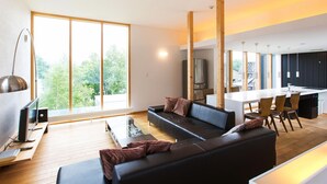 Un salon moderne avec un canapé noir, une table basse en bois et un téléviseur. On y trouve également un coin repas avec un grand îlot et des chaises.