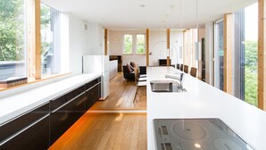 Une cuisine moderne dotée d’un long comptoir, d’une cuisinière encastrée et offrant une vue sur l’extérieur grâce à de grandes fenêtres.
