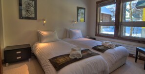 Une chambre d’hôtel avec deux lits, une table de chevet, un bureau et une fenêtre donnant sur un paysage enneigé.