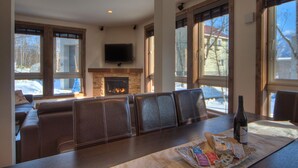 A cozy living room with a fireplace, large windows, and a dining area with a table set for two.