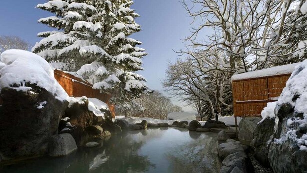 A serene winter scene with a snow-covered landscape, a clear pond, and traditional wooden structures.
