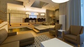 A modern living room with a sofa, armchair, and coffee table. There is a staircase leading to an upper level, and a dining area with chairs and a table.
