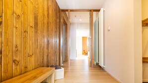 A hallway with wooden paneling on one side, a bench with a basket, and a coat rack on the other. - Luxury 5 Star 3 Bedroom Chalet, Niseko Chalet 1005 (Niseko)