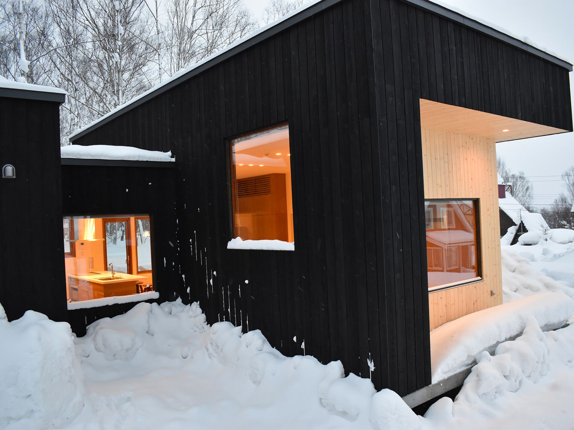 A modern house with large windows, surrounded by snow.