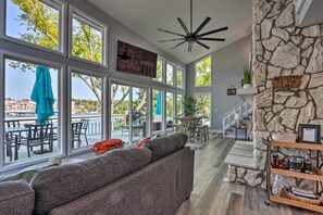 A spacious living area with a large gray sofa, a stone accent wall, and a view of the outdoors. - Boat Dock, Furnished Deck! Lakefront Ozarks Home (Lake Ozark)