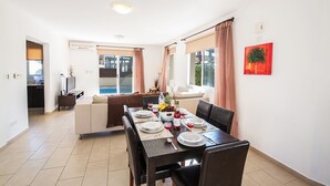 A dining area with a table set for four, a sofa, and a view of the outdoors. - Beautiful 5 Star Holiday Villa in a Prime Location in Protaras (Paralimni)