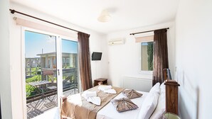 A hotel room with a bed, a TV, a window with curtains, a radiator, and a view of the outside. - Beautiful 5 Star Holiday Villa in a Prime Location in Protaras (Paralimni)
