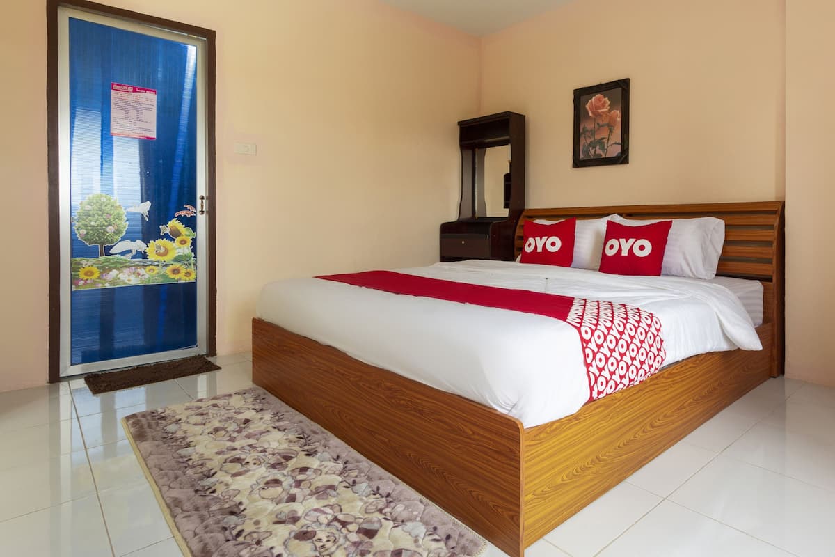 Une chambre avec un lit en bois, une literie blanche, un plaid rouge et un tapis à motifs floraux.