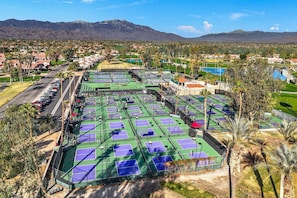 Ett tenniscenter med flera banor, omgivet av bostadshus och med ett bergigt landskap i bakgrunden.