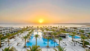 A resort with multiple swimming pools, palm trees, and a view of the sunset over the ocean.