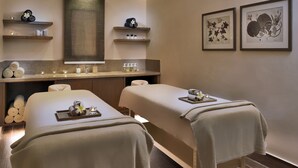 Un cuarto de spa con dos camillas de masaje, toallas, velas e impresiones enmarcadas de motivos botánicos en la pared.