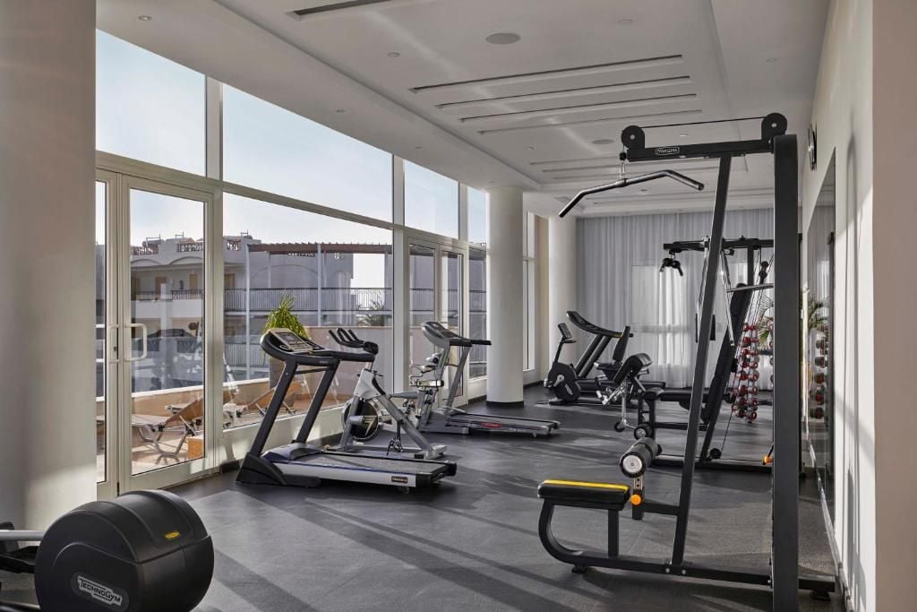 Une salle de sport moderne équipée de machines de cardio, de poids libres et d’un miroir.